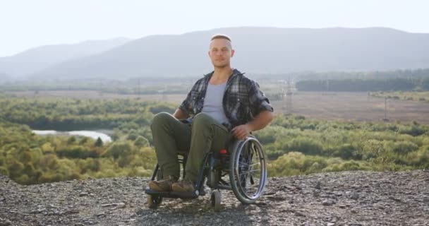 Красивий вдумливий 30-річний хлопець-неприпустимий у позі інвалідного візка на камеру з схрещеними руками на горі на тлі красивих пейзажів — стокове відео