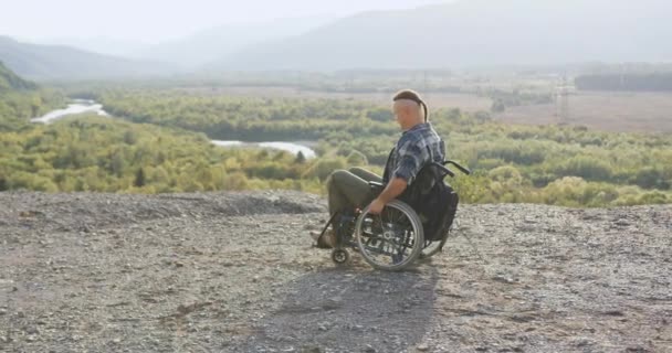 Vista lateral de atraente jovem moderno deficiente homem em cadeira de rodas que olhando ao redor no topo da colina para as paisagens pitorescas — Vídeo de Stock