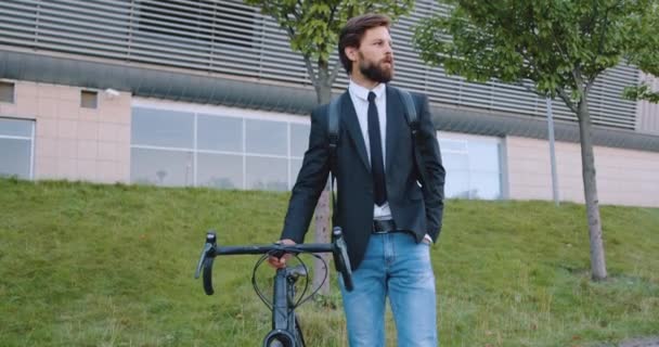 Vue de face d'un bel homme barbu équilibré et confiant de 30 ans vêtu d'une veste sombre et d'un jean assorti à son vélo dans la rue — Video
