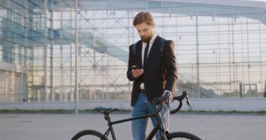 Yakışıklı özgüvenli başarılı, düşünceli, sakallı ofis yöneticisinin portresi büyük cam binanın önünde duruyor ve telefonda birine mesaj yazıyor.