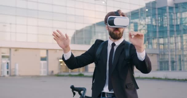 Vista frontal de apuesto gerente de oficina barbudo joven con propósito seguro en gafas de realidad aumentada que trabajan en la pantalla imaginaria cerca del edificio de vidrio moderno — Vídeos de Stock