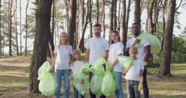 Çöp torbalarıyla parkın ortasında durup kameraya poz veren iyi görünümlü aktif ırk gönüllülerinin portresi.