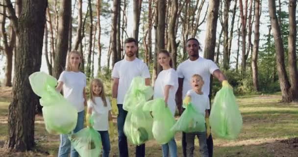 Positieve actieve gemengde ras natuurliefhebbers poseren op camera met plastic zakken met afval dat ze verzameld over het hele park, de samenleving tegen vervuiling concept — Stockvideo
