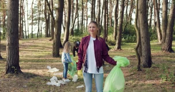 People against pollution when attractive positive young woman posing on camera with collected rubbish near another friends-activists of nature lovers — Stock Video