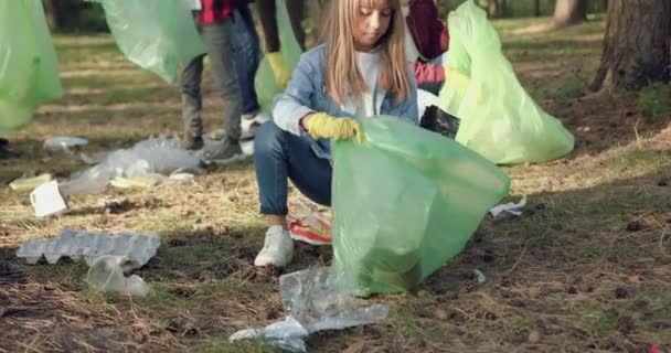 Vonzó, koncentrált gyerekek portréja felnőttekkel, akik műanyag dobozokat tartanak a kezükben, és szemetet szednek fel beléjük a park minden tájáról. — Stock videók