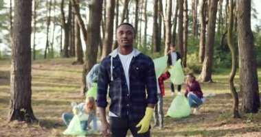 İyi huylu Afro-Amerikan vatandaşları kameranın önünde doğa sever arkadaşlarının yanında duruyor. Orman bölgesinden toplanan çöpleri plastik torbalara dolduruyorlar.