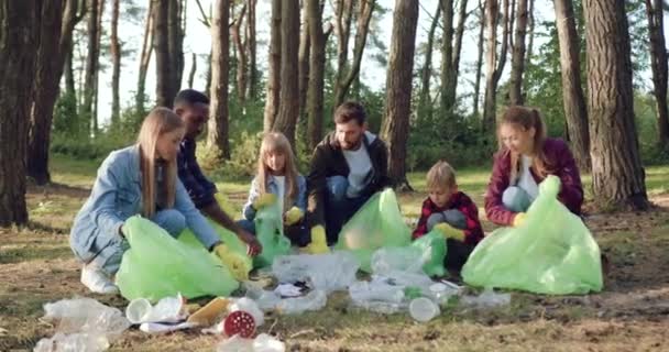 Vista frontale di simpatico gruppo attivo di adulti e bambini che puliscono il parco dalla spazzatura per mantenere la natura in bellezza e pulizia — Video Stock