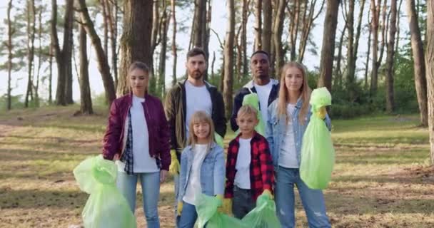 Framifrån av sympatisk aktiv vänlig ung grupp av naturälskare som poserar på kameran med plastpåsar fulla av avfall som de samlat ihop från parkens territorium — Stockvideo