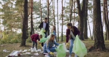 Güzel, tatmin olmuş aktif kadın gönüllüler park bölgesinden plastik torbalara çöp topluyor ve çalışanların arka planında birbirlerine beşlik çakıyorlar.