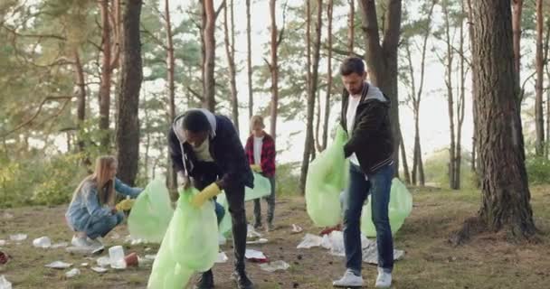 Przystojni, ciężko pracujący, wielorasowi mężczyźni pomagają zbierać śmieci do plastikowych toreb. Ich przyjaciele-aktywiści natury i przybijają sobie piątkę. Społeczeństwo przeciwko zanieczyszczeniom. — Wideo stockowe