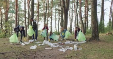 İyi görünümlü, genç, etkin, koruyucu eldivenli yetişkinler ve çocuklardan oluşan bir ekip çöpleri plastik torbalara dolduruyor. Kirliliğe karşı toplum.
