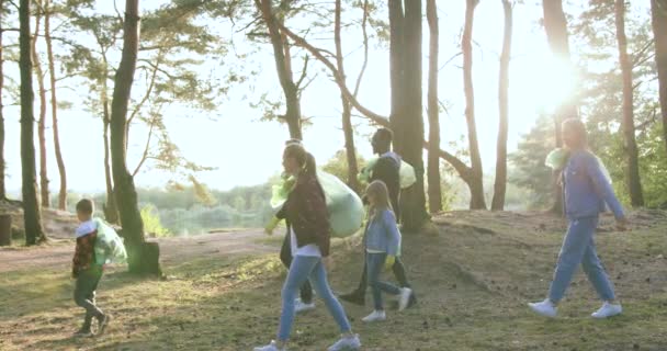 Buen carácter satisfecho voluntarios activos diversos con bolsas de basura salir del parque después de la limpieza de otoño, cámara lenta — Vídeos de Stock