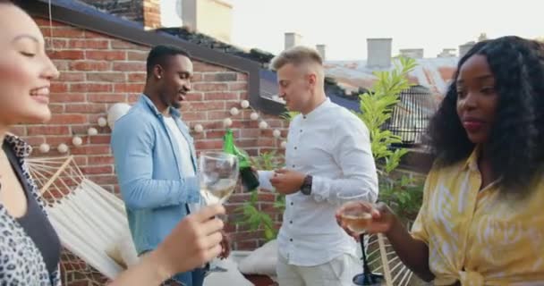 Привабливі позитивні багатоетнічні друзі розважаються разом на балконі, п'ють пиво і вино і посміхаються багато під час літньої вечірки, крупним планом — стокове відео