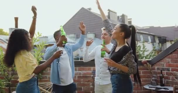 Portrait of good-natured smiling lucky 25s multiethnic friends which gethering together to celebrate summer party on the balcony with dances and beer and wine — Stock Video