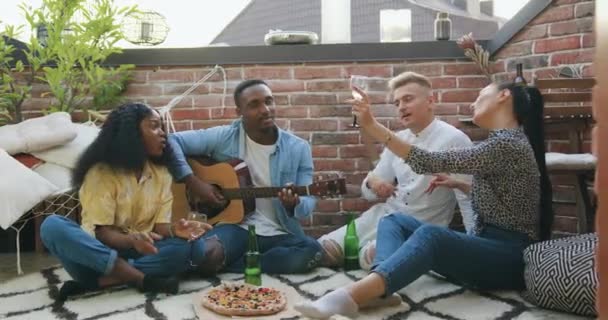 현대 혼혈인 현대 혼혈의 좋은 기질에 대한 정면의 전망은 기타, 음료 및 여름 파티 동안 음식에서 노래와 함께 테라스에서 그들의 공동 레저를 즐기는 젊은 만족 — 비디오