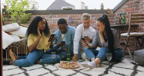 Portrait d'attrayant confiant 25s multiracial meilleurs amis qui assis sur le balcon sur le tapis et en utilisant leurs smartphones en attendant quelqu'un — Video
