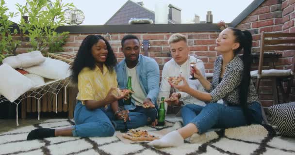Blisko atrakcyjnych szczęśliwych młodych przyjaciół wielorasowych, którzy odpoczywają na balkonie i piją wino, piwo i jedzą pizzę podczas letniej imprezy — Wideo stockowe