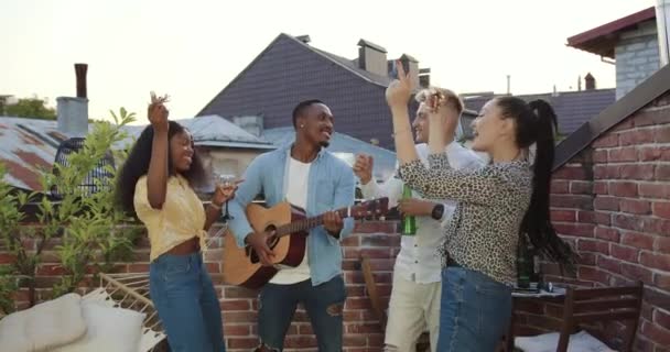 Yüksek moralli çok ırklı gençlerin gitar müziği eşliğinde ellerini kaldırarak dans etmesi, kafalarının üstüne konfeti kusması ve yaz partisinde terasta içki içmesi çok çekici. — Stok video