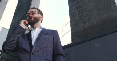 İyi görünümlü, kendine güvenen, 35 yaşında, gözlüklü bir iş adamının ön görüntüsü. Ofis merkezinin merdivenlerinde duruyor ve ortağıyla gezici bir konuşma yapıyor.