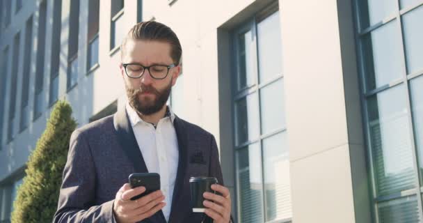 Un homme d'affaires barbu de 35 ans en costume officiel a un appel téléphonique pendant l'heure du café près de l'immeuble de la grande ville, ralenti — Video