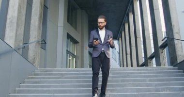 İş konsepti. Güzel görünüşlü, kendine güvenen, şık giyimli iş adamı. Ofisten çıkarken merdivenlerden inip telefonla konuşuyor.