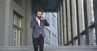 Gözlüklü ve şık takım elbiseli çekici, kendine güveni tam bir yetişkin ofis çalışanı kahve içip telefonla konuşurken merdivenlerden çıkarken...