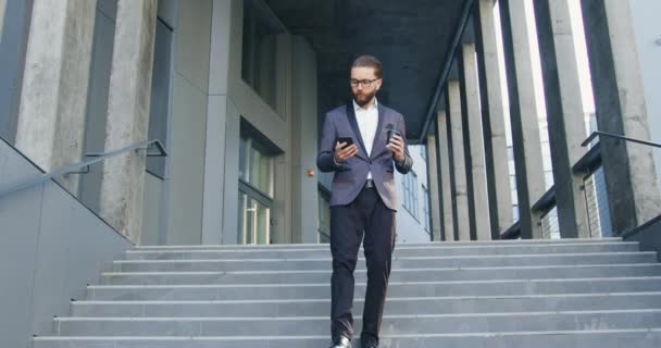 Concept d'affaires où beau confiant concentré homme d'affaires barbu dans des vêtements élégants descendant les marches tout en quittant le centre de bureau et parler au téléphone — Video