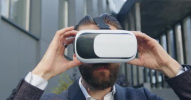 Yakışıklı, kendine güveni tam sakallı adam sanal gerçeklik kulaklığı takıyor ve şehir modern binasının yanında çalışmaya başlıyor.