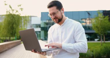 Laptop kullanan, Webinars izleyen, uzaktan kumandalı, e-ticareti internetten öğrenen, modern cam bina arka planında başarılı bir beyaz adam. Yavaş çekim