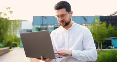 Yakışıklı adam metin yazarının portresi dizüstü bilgisayar kullanıyor, daktilo yazıyor, internette serbest çalışıyor, açık havada çalışıyor. Yavaş çekim