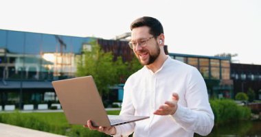 Laptop bilgisayar iletişimini kullanan kendine güvenen beyaz bir adamın portresi, açık havada görüntülü konuşma. Yavaş çekim