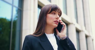 Cam ofis binasının yakınındaki akıllı telefonuyla konuşan kendine güvenen esmer bir bayanı yakından çek. Profesyonel ve ciddi ifade, şehir geçmişi. Yavaş çekim