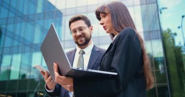 İki iş arkadaşı şirket binasının girişinde dizüstü bilgisayar kullanarak sohbet ediyorlar. İş adamları ve iş toplantıları. Yavaş çekim