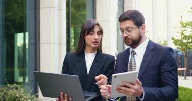 Elinde tablet bulunan başarılı erkek arkadaşıyla birlikte bir şehir bölgesinde yürürken, odaklanmış iş kadınının işaret ettiği dizüstü bilgisayarın ekranını kapatın. Birlikte yeni bir projeyi tartışıyorlar. Açık hava, Ağır çekim