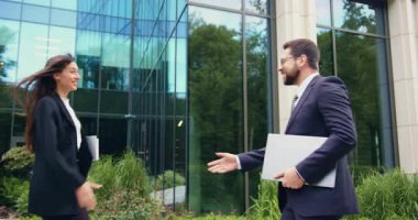 İki iş ortağının yakın çekimi, resmi takım elbiseli bir adam ve bir kadın, şehirdeki bir ofis binasının yakınında el sıkışarak birbirlerini selamlıyorlar..