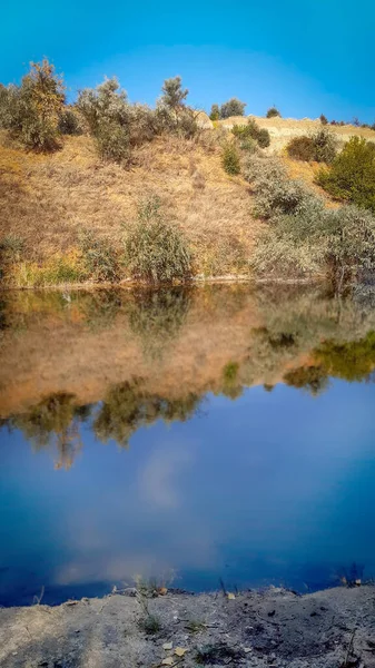 Krajobraz brzeg rzeki z żółtymi zielonymi drzewami w letni dzień odzwierciedlone w wodzie — Zdjęcie stockowe