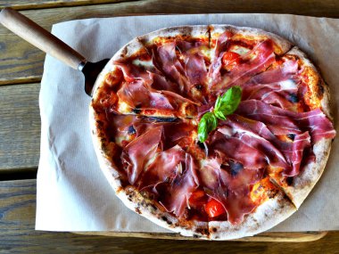 Pastırma, domates, hizmet için bir spatula ile ahşap bir masa üzerinde otlar İtalyan pizza. yakın çekim. pizza restoran kavramı.