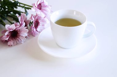 Bir fincan çay ve pembe Krizantem çiçeği masanın üzerinde. Arka plan bulanık.