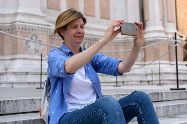 İnce, ince orta yaşlı bir kadın, Bologna, İtalya için turist. Şehir ve Fotoğraf Merkezi Meydanı'nda San Petronio Bazilikası adımları Smartphone oturur. Avrupa'ya seyahat.
