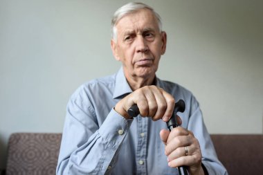 Elleri evde oturan bir baston eğilerek düşünceli bir adam. Yaşlanma, hastalık, depresyon, yaşlılık yalnızlık.