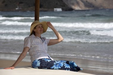 Bir plaj çardak oturan orta yaşlı kadın, deniz izliyor.