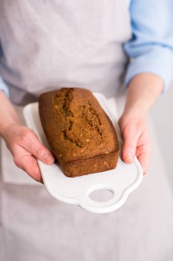 Kadın eli taze pişmiş kek, tahıl ve tohumlu ekmek tutuyor. Ev yapımı kekler seramik bir tahtada servis edilir..