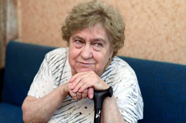 Çubuğa yaslanmış üzgün, yaşlı bir kadının yakın plan portresi..