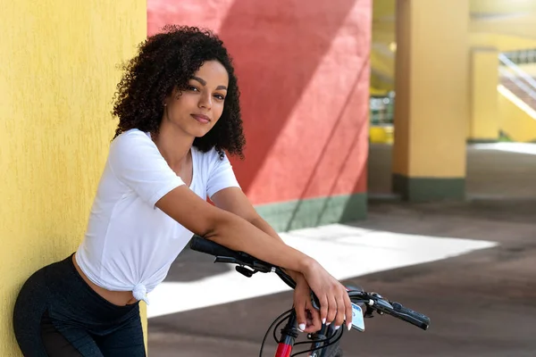 Çekici, narin, Afro-Amerikan kadın spor giyimli, bisikletli, şehirde bir sokakta..