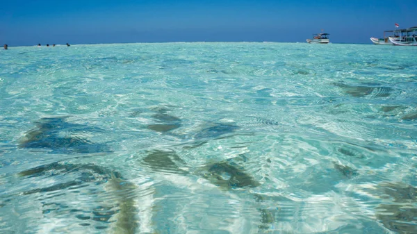 a clear and clean sea water in shallow area with people swimming and traditional boat in distance in karimun jawa indonesia