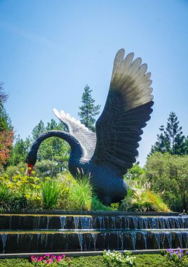 big black swan statue on green forest and grass with blue sky - photo