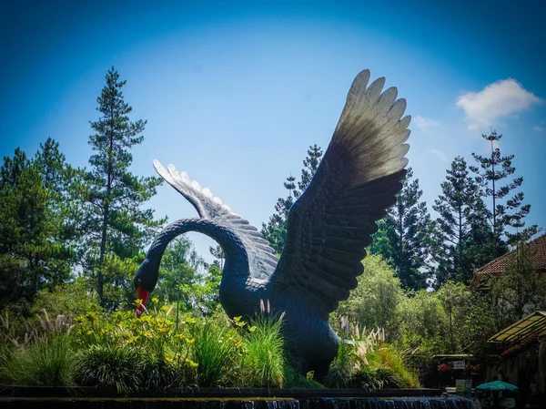 big black swan statue on green forest and grass with blue sky - photo