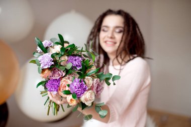 Bir buket çiçek elinde kapalı gösterilen dreadlocks saç modeli ile gülümseyen kız. Arka plan üzerinde bulanık kızla çiçekler üzerinde odaklanmak.