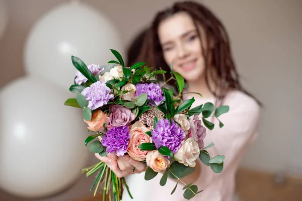 Smiling girl with dreadlocks hairstyle showing a bouquet of flowers in hands indoors. Focus on flowers with blurred girl  on background.