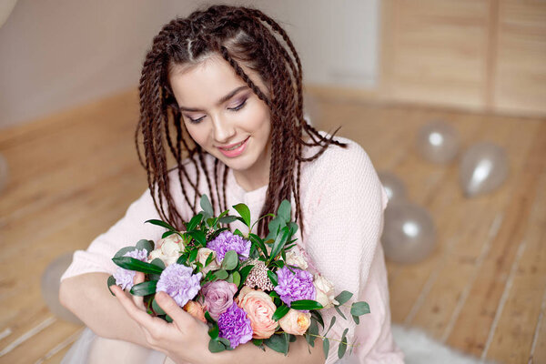 Close up view of beautiful teen girl with dreadlocks hairstyle holding a bouquet of flowers indoors 
